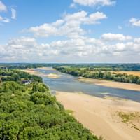 Luftaufnahme der Loire, die durch französische Landschaft fließt mit Sandbänken, grünen Wäldern und Feldern unter bewölktem Himmel.