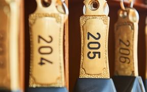 Vintage-Hotelzimmerschlüssel mit beigen Lederanhängern mit den Nummern 204, 205 und 206, die an Metallhaken an einem Holzschlüsselbrett hängen.