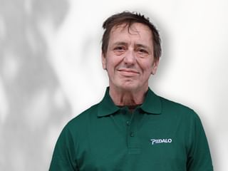 Porträt von Gerhard Wamser in einem grünen Poloshirt mit Pedalo-Logo, lächelnd vor weißem Hintergrund.