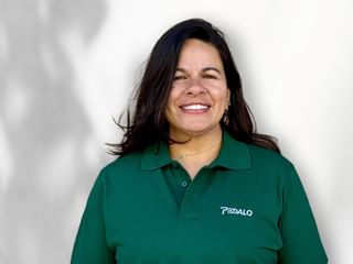 Portrait of a smiling woman with long dark hair wearing a green polo shirt with Pedalo logo, standing against a white background.