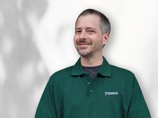 Porträt von Grigorij Kuklin in einem grünen Pedalo-Poloshirt, lächelnd zur Seite blickend vor weißem Hintergrund.