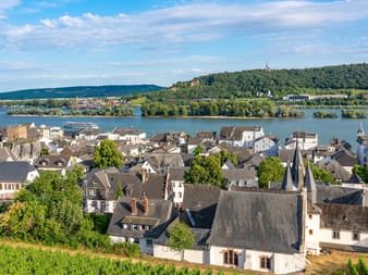 Aerial view of a historic Rhine River town with traditional German architecture, church spires, and river cruise ship on the water.