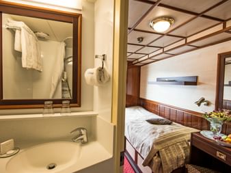 Innenraum der Florentina Schiffskabine mit Badezimmer mit Waschbecken, Spiegel und Dusche, plus Schlafbereich mit Einzelbett und Obstschale.