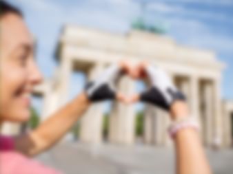 Frau in pinkem Oberteil fotografiert mit Smartphone das Brandenburger Tor in Berlin. Das berühmte Wahrzeichen ist im Hintergrund sichtbar.