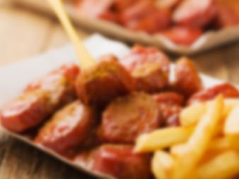 Geschnittene Currywurst mit Curry-Ketchup-Sauce und Pommes frites serviert auf einem mit Papier ausgelegten Tablett mit Holzgabel.