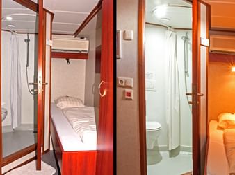 Innenansicht der Zwantje Schiffskabine mit Einzelbett mit gestreifter Bettwäsche, kompaktem Bad mit Dusche und WC, warmer Holzvertäfelung.