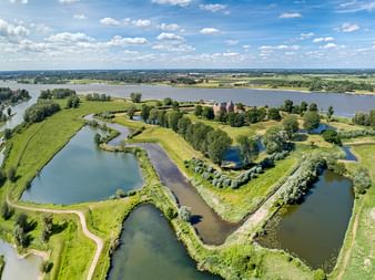 Aerial view of Dutch Water Line with star-shaped water fortifications, green meadows, and a red brick castle surrounded by waterways.