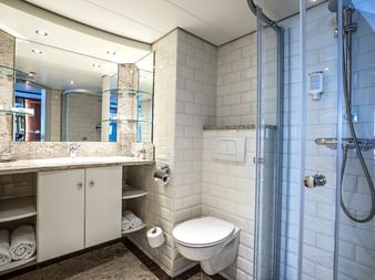Modernes Schiffsbadezimmer mit weißen U-Bahn-Fliesen, Glasdusche, Granit-Waschtisch, wandhängendem WC und Spiegel mit Stauraum.