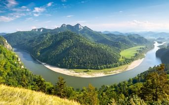 Luftaufnahme des Dunajec-Flusses, der eine dramatische Hufeisenbiegung durch bewaldete Berge mit Felsgipfeln unter blauem Himmel bildet.
