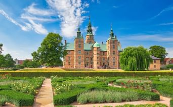 Rotes Backsteinschloss Rosenborg mit grünen Kupfertürmen in Kopenhagen, umgeben von barocken Gärten mit geometrischen Hecken.