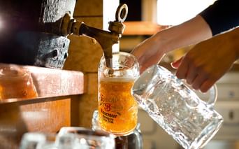 Nahaufnahme von Bier, das aus einem Messinghahn in einen traditionellen Glaskrug gezapft wird. Eine Hand hält einen leeren Krug daneben.