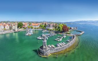 Luftaufnahme des Lindauer Hafens am Bodensee mit Steinmole, Löwenstatue, Leuchtturm, Yachthafen und historischer Altstadt.