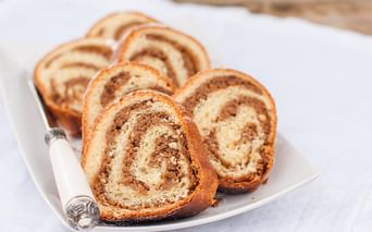 Geschnittene süße Brotrolle mit spiralförmiger Nussfüllung auf einem weißen Teller. Das goldbraune Gebäck zeigt abwechselnde Teig- und Füllungsschichten.