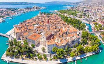 Luftaufnahme einer dalmatinischen Küstenstadt Luftaufnahme einer historischen dalmatinischen Küstenstadt mit orangefarbenen Ziegeldächern, Glockenturm und türkisfarbenem Hafen.