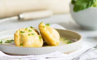 Drei geschälte Salzkartoffeln auf einem weißen Teller, mit zerlassener Butter und gehacktem Schnittlauch garniert. Im Hintergrund ist eine Schüssel mit frischem Grün sichtbar.