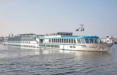 Weißes Flusskreuzfahrtschiff Swiss Crown mit blauen Akzenten auf ruhigem Wasser. Das mehrstöckige Schiff hat große Fenster und eine niederländische Flagge.