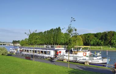 Weißes Passagierschiff Zwantje am Flussufer festgemacht mit aufgereihten Fahrrädern auf dem Pier. Grüne Wiese und Bäume im Hintergrund.