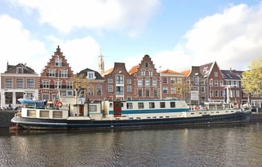 Großes weiß-blaues historisches Schiff Flora am Kanal vor traditionellen holländischen Giebelhäusern und einem Kirchturm.