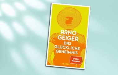 Buchcover von Arno Geiger mit dem Titel 'Das glückliche Geheimnis' in gelb-oranger Gestaltung mit einer Figur mit sonnenähnlichem Gesicht und Hut.