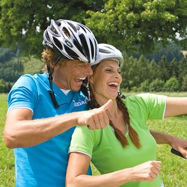 Happy cycling couple with helmets outdoors Two smiling cyclists wearing helmets embrace in a green park setting. The man wears a blue shirt, the woman a green shirt.