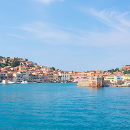 Panoramablick auf eine farbenfrohe Küstenstadt an der Toskanischen Küste mit historischen Gebäuden und Festungsmauern im türkisfarbenen Wasser.
