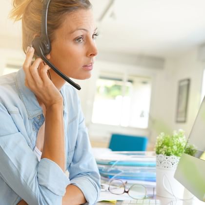 Frau mit Headset arbeitet am Computer in hellem Büro. Sie trägt ein hellblaues Hemd und konzentriert sich auf den Bildschirm.