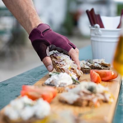 Hand greift nach Appetithäppchen auf einem Holzbrett mit Brot, Aufstrichen und Tomaten, begleitet von zwei Gläsern Bier in Oberösterreich.
