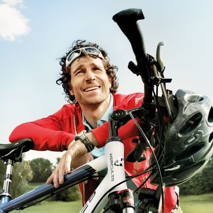 Lächelnder Radfahrer in roter Jacke mit weißem Fahrrad und Helm auf grüner Wiese unter blauem Himmel im Spreewald.
