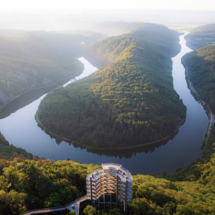 Aerial view of the Saar River forming a horseshoe bend through forested hills in Saarland. A viewing platform is visible in the foreground.