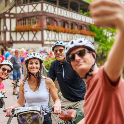 Gruppe von fünf Radfahrern mit Helmen macht ein Selfie vor traditionellen Fachwerkhäusern entlang eines Kanals in Straßburg.