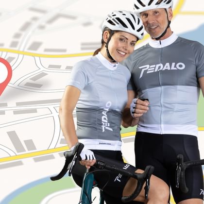 Two smiling cyclists in helmets and cycling jerseys holding road bikes, standing in front of a stylized map with a red location pin.