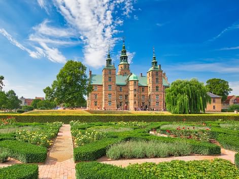 Rotes Backsteinschloss Rosenborg mit grünen Kupfertürmen in Kopenhagen, umgeben von barocken Gärten mit geometrischen Hecken.