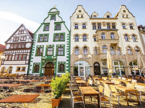Bunte historische Gebäude in Thüringen mit Außengastronomie. Grünes Barockgebäude und cremefarbene Renaissancefassaden säumen den Platz.