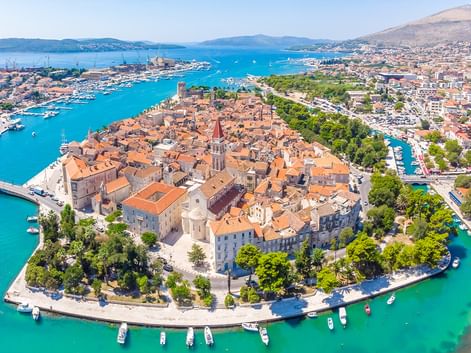 Luftaufnahme einer dalmatinischen Küstenstadt Luftaufnahme einer historischen dalmatinischen Küstenstadt mit orangefarbenen Ziegeldächern, Glockenturm und türkisfarbenem Hafen.