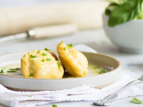 Drei geschälte Salzkartoffeln auf einem weißen Teller, mit zerlassener Butter und gehacktem Schnittlauch garniert. Im Hintergrund ist eine Schüssel mit frischem Grün sichtbar.