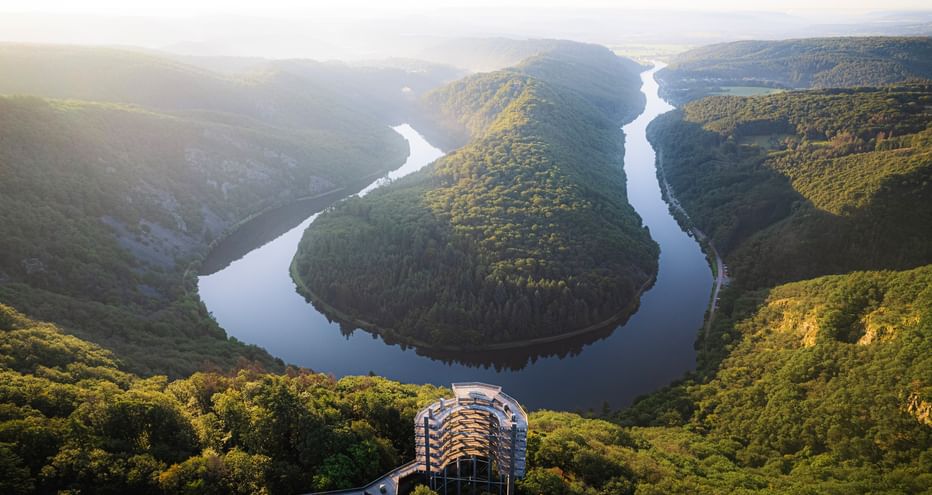 Aerial view of the Saar River forming a horseshoe bend through forested hills in Saarland. A viewing platform is visible in the foreground.