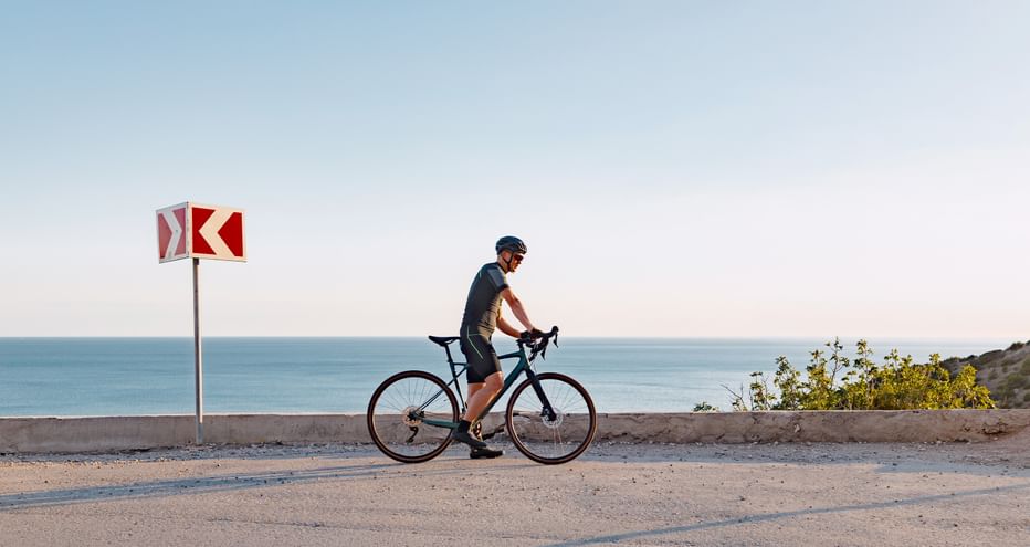 Radfahrer mit Rennrad auf Küstenstraße in der Algarve mit Meerblick, rot-weißem Verkehrsschild und klarem blauen Himmel.