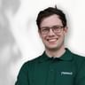 Portrait von Sandi mit Brille und grünem Pedalo-Poloshirt, lächelnd vor weißem Hintergrund.