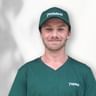 Porträt von Aidan mit grüner Pedalo-Kappe und passendem V-Ausschnitt-Shirt mit Pedalo-Logo, lächelnd vor weißem Hintergrund.